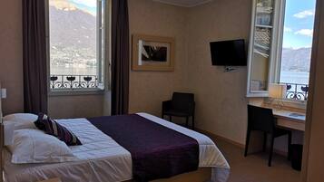 Une chambre d’hôtel équipée d’un lit, d’un bureau, d’une chaise, d’une télévision et d’une fenêtre donnant sur les montagnes.