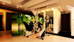 Un gimnasio con bicicletas estáticas y una caminadora, un reloj y una puerta con un letrero rojo de salida de emergencia.