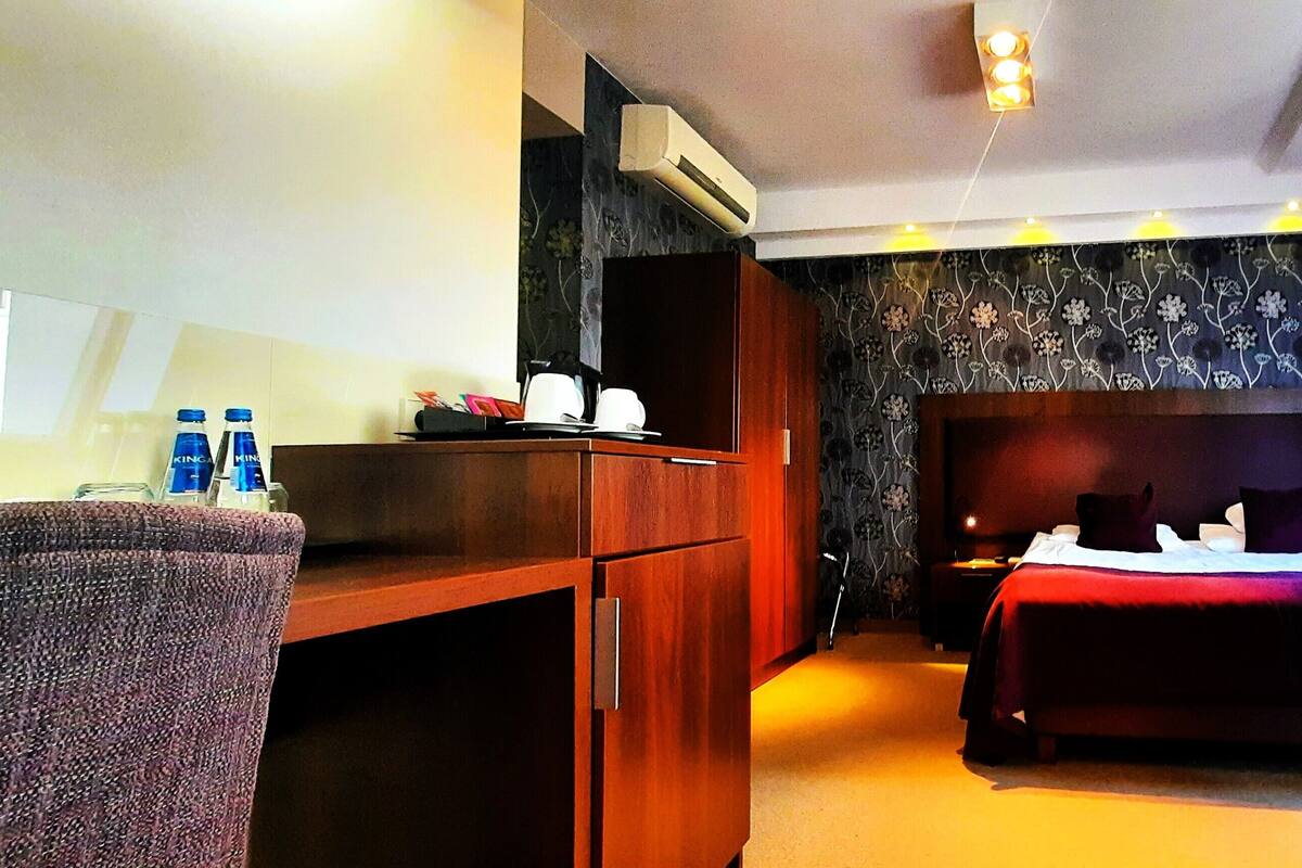 A hotel room with a bed, a desk, a chair, a small table, and a window.