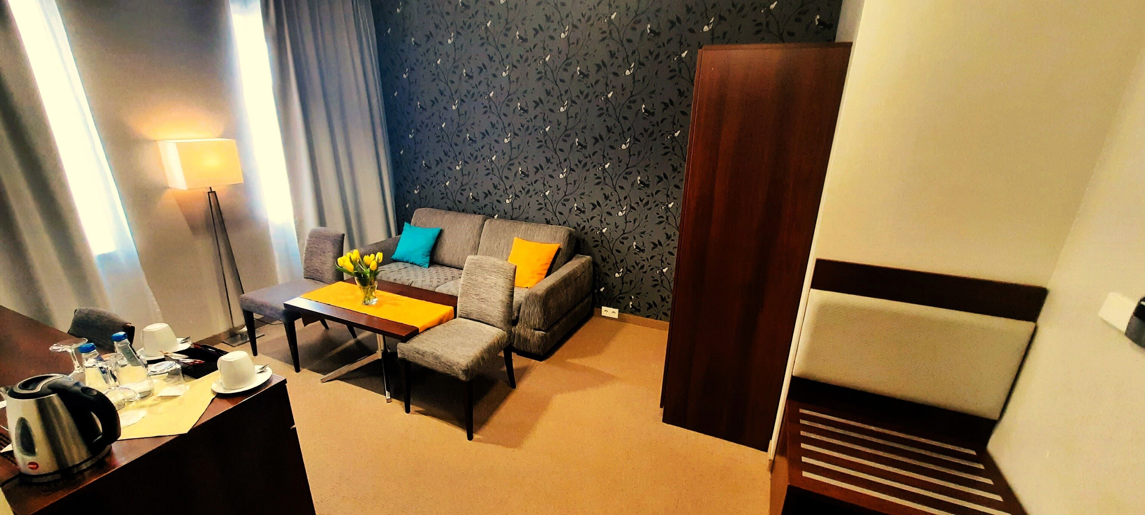 Ett hotellrum med en soffa, ett soffbord, ett skrivbord med en vattenkokare och koppar samt en lampa.