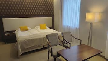 A hotel room with a bed, two chairs, a table, and a lamp.