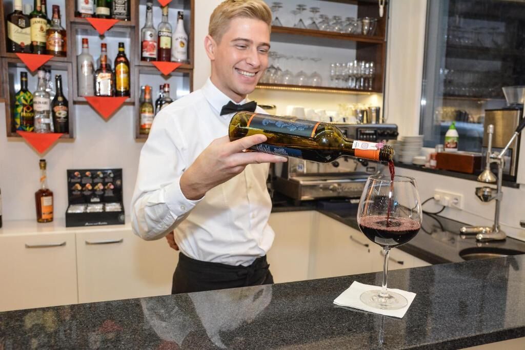 A bartender pouring wine into a glass.