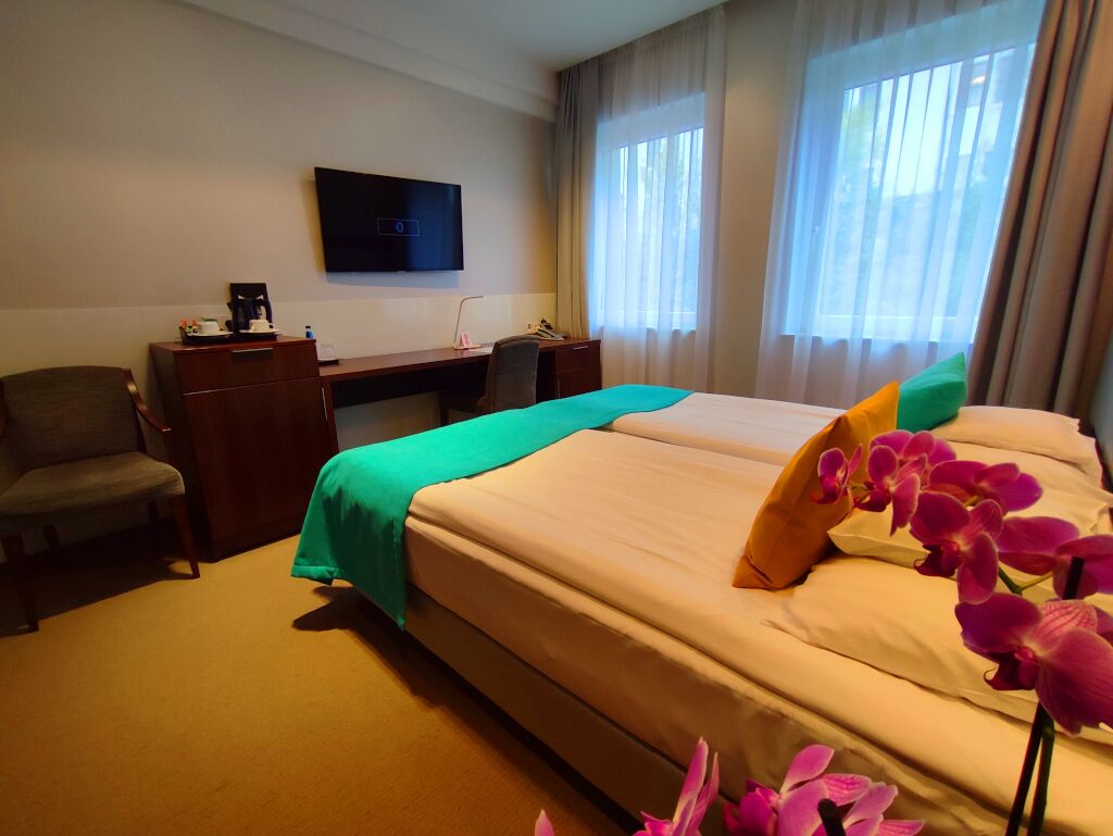 A hotel room with a bed, a desk, a chair, a TV, and curtains.