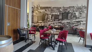 Un restaurante con un gran mural de la ciudad en la pared, sillas tapizadas en rojo y un barril de madera.