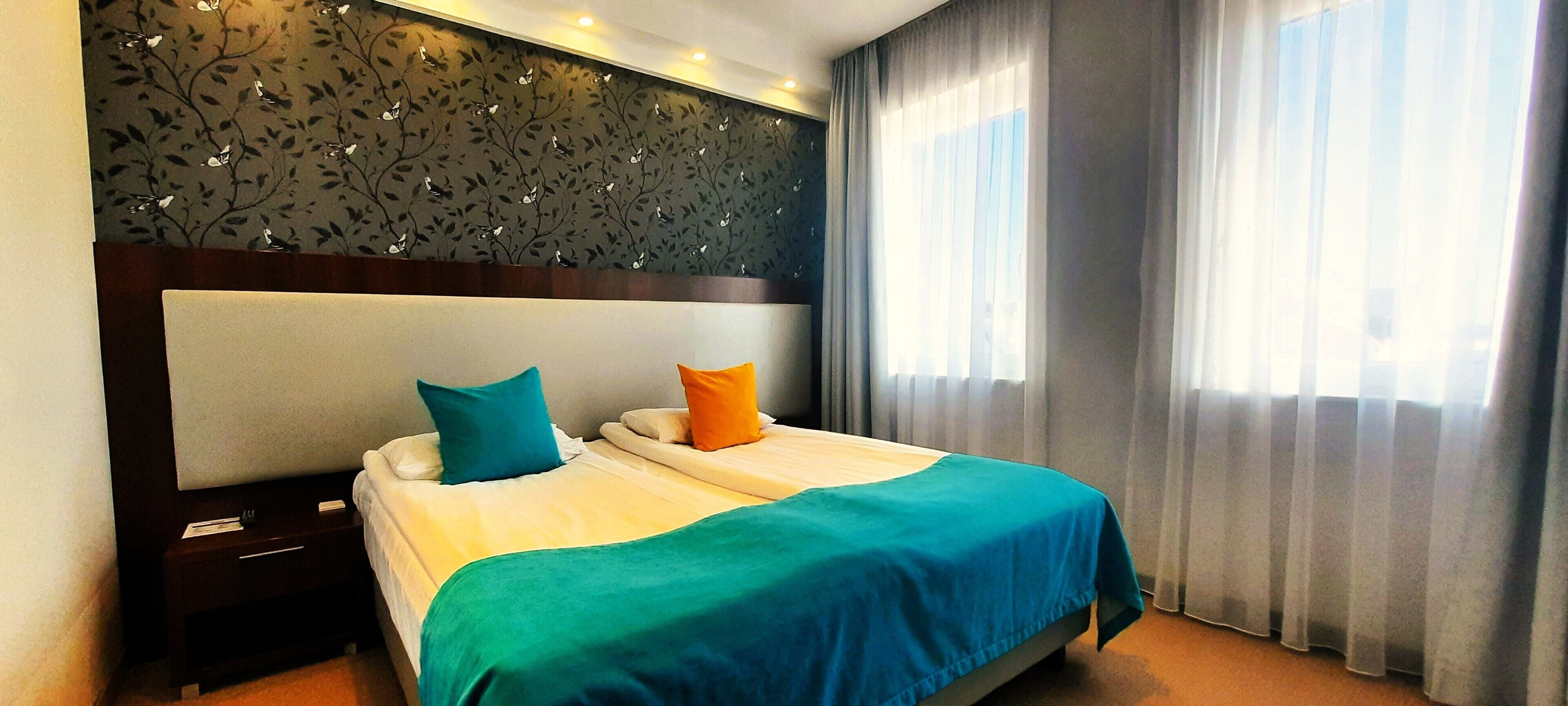 A hotel room with a large bed, two pillows, a nightstand, and a decorative wall panel.