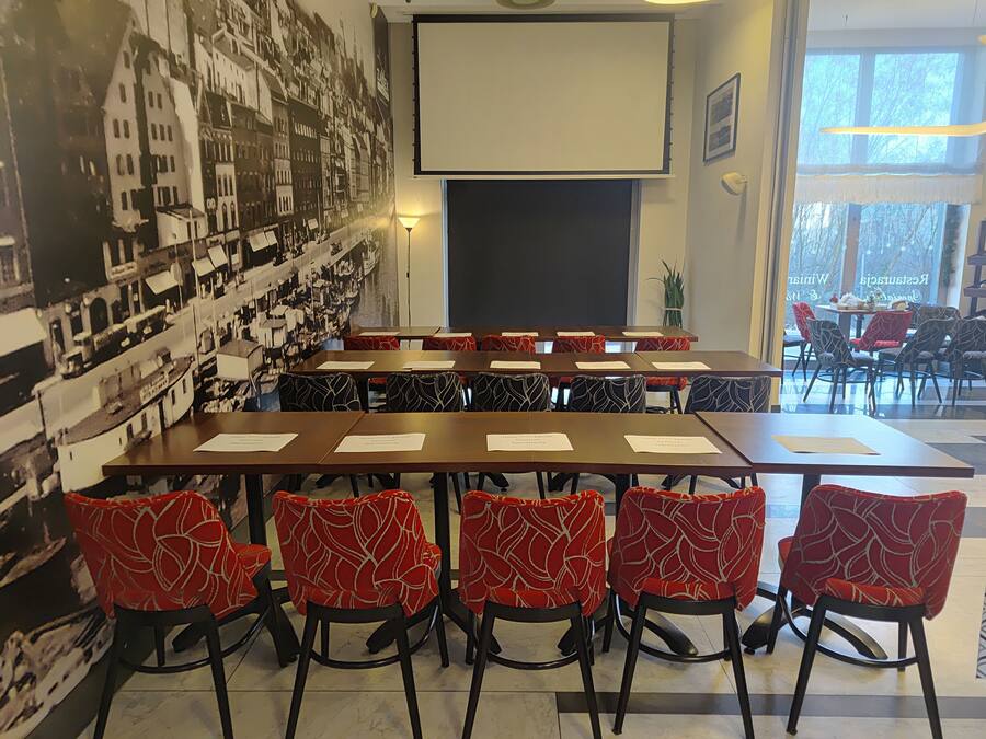 Een vergaderzaal met een groot projectiescherm, rode gestreepte stoelen en een stadsgezicht muurschildering.