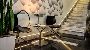 Un interior moderno con una escalera, una mesa de vidrio con sillas y una pared decorativa.