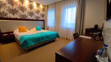 Quarto de hotel com cama, escrivaninha, cadeira e televisão.