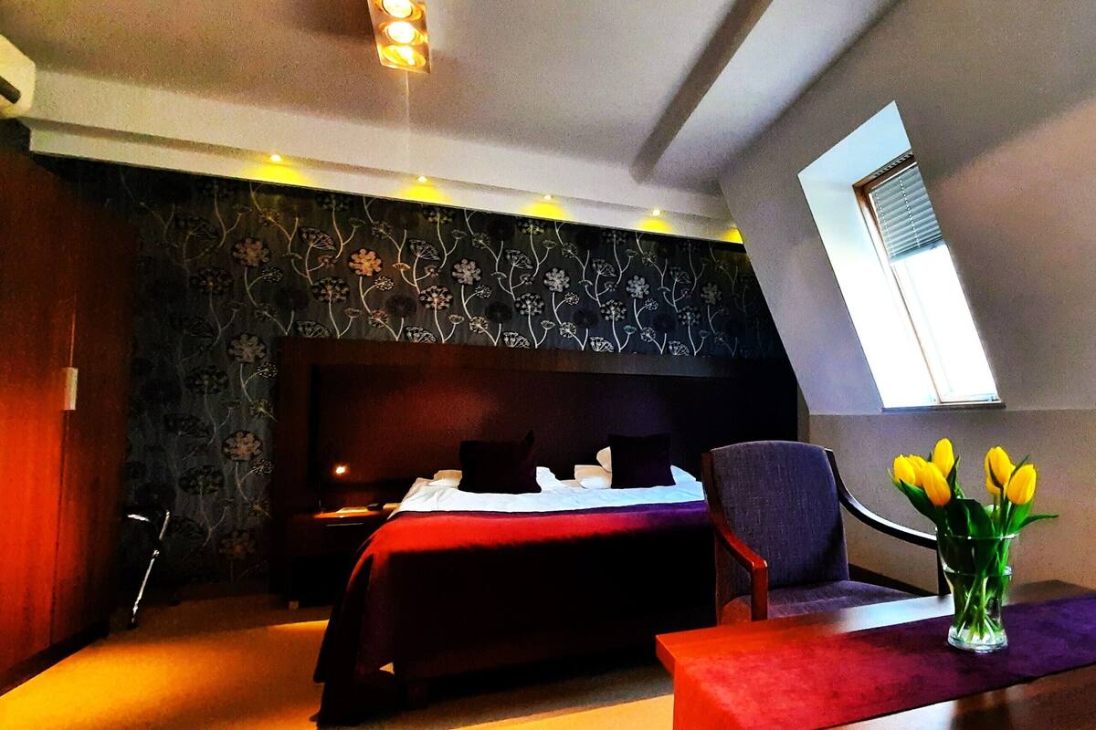A bedroom with a bed, a chair, a table, and a vase with flowers.
