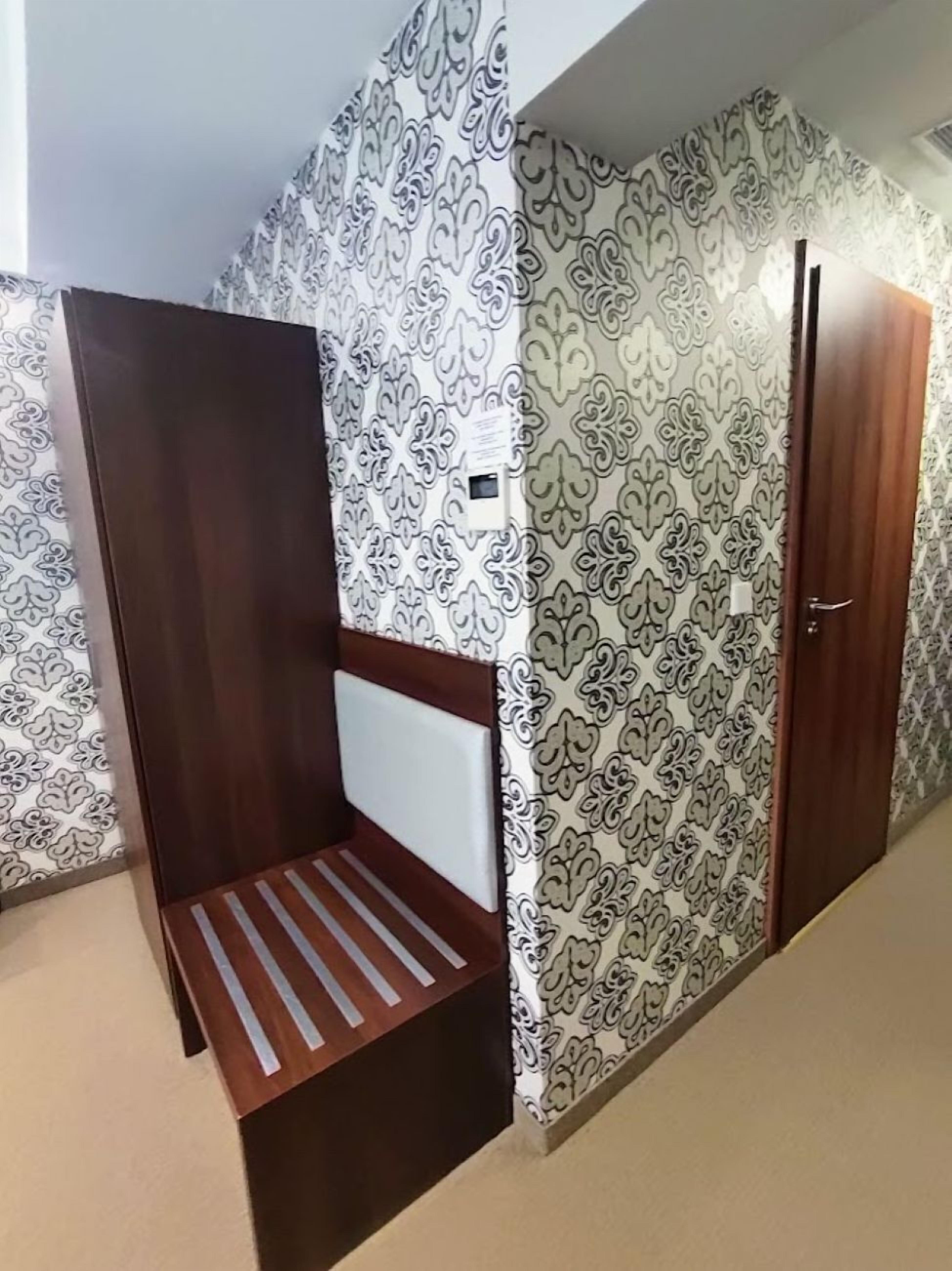 A room with a patterned wallpaper, a wooden bench, and a door.
