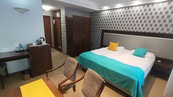 Una habitación de hotel con una cama, un escritorio, una silla, un armario y una mesita de noche.
