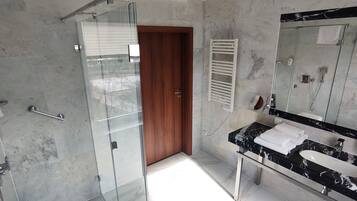 A modern bathroom with a glass shower door, a wooden door, a marble sink, and a large mirror.