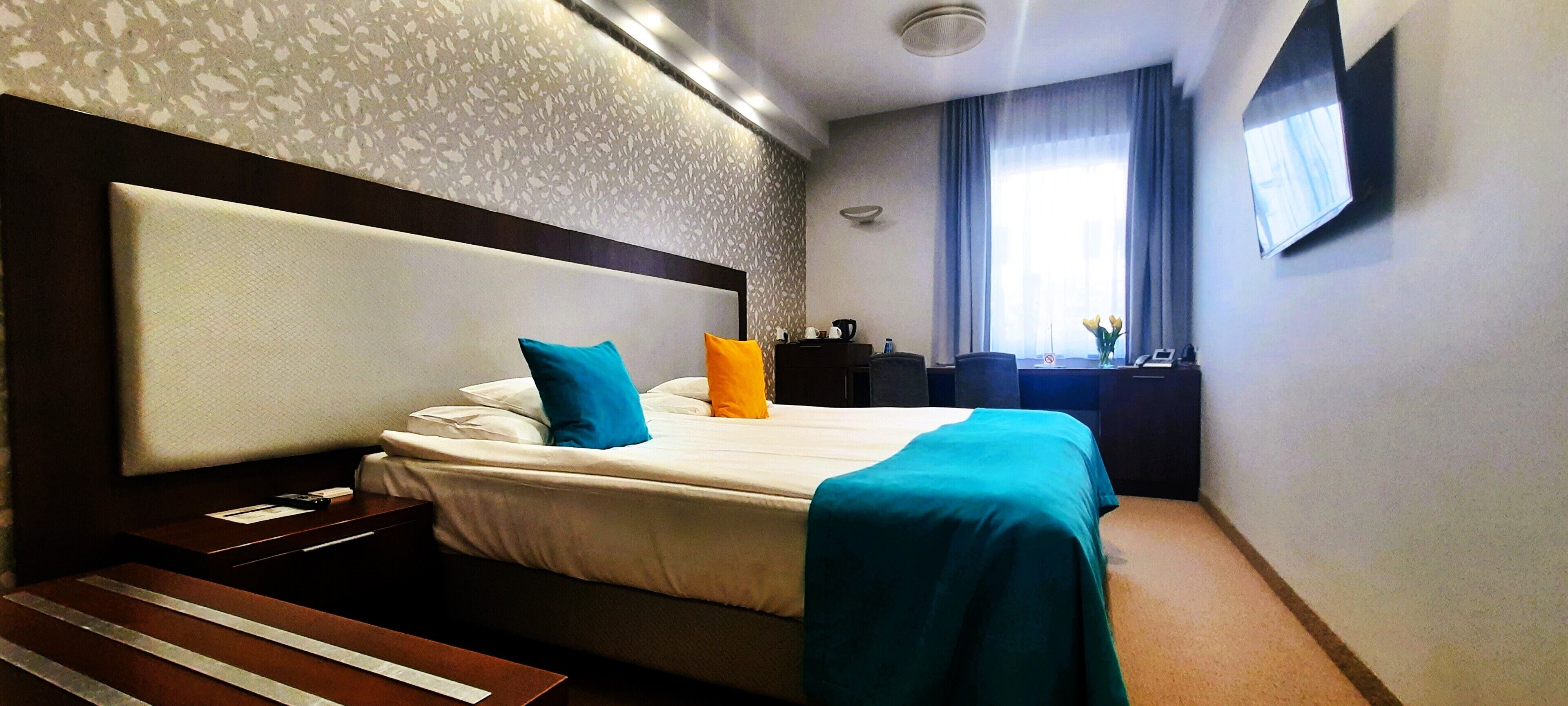 A hotel room with a large bed, a desk, a chair, a TV, and a window with curtains.