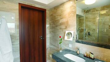 A modern bathroom with a marble wall, a wooden door, a large mirror, and a white sink.