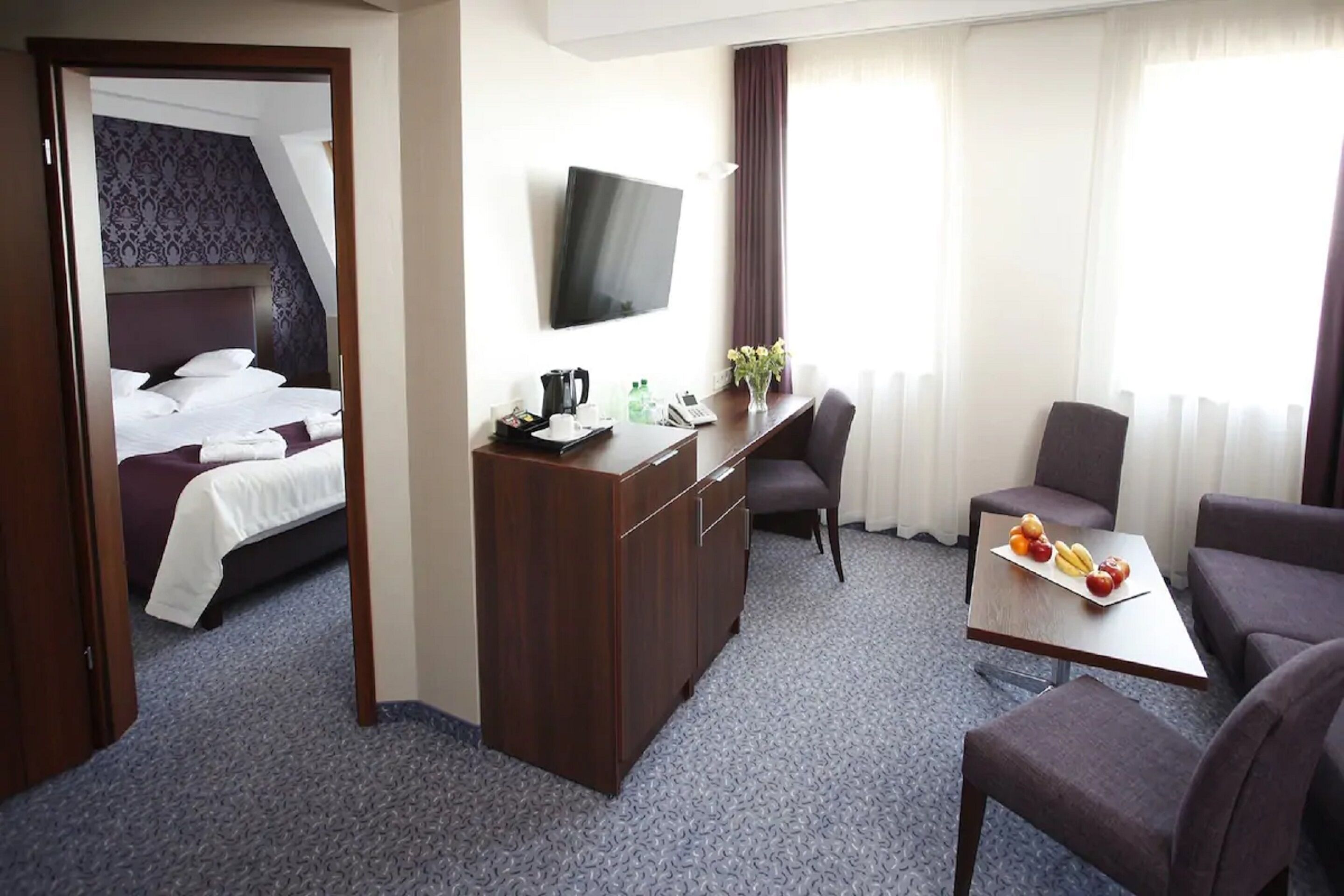 A hotel room with a bed, a desk with a flat-screen TV, a coffee maker, and a fruit plate.
