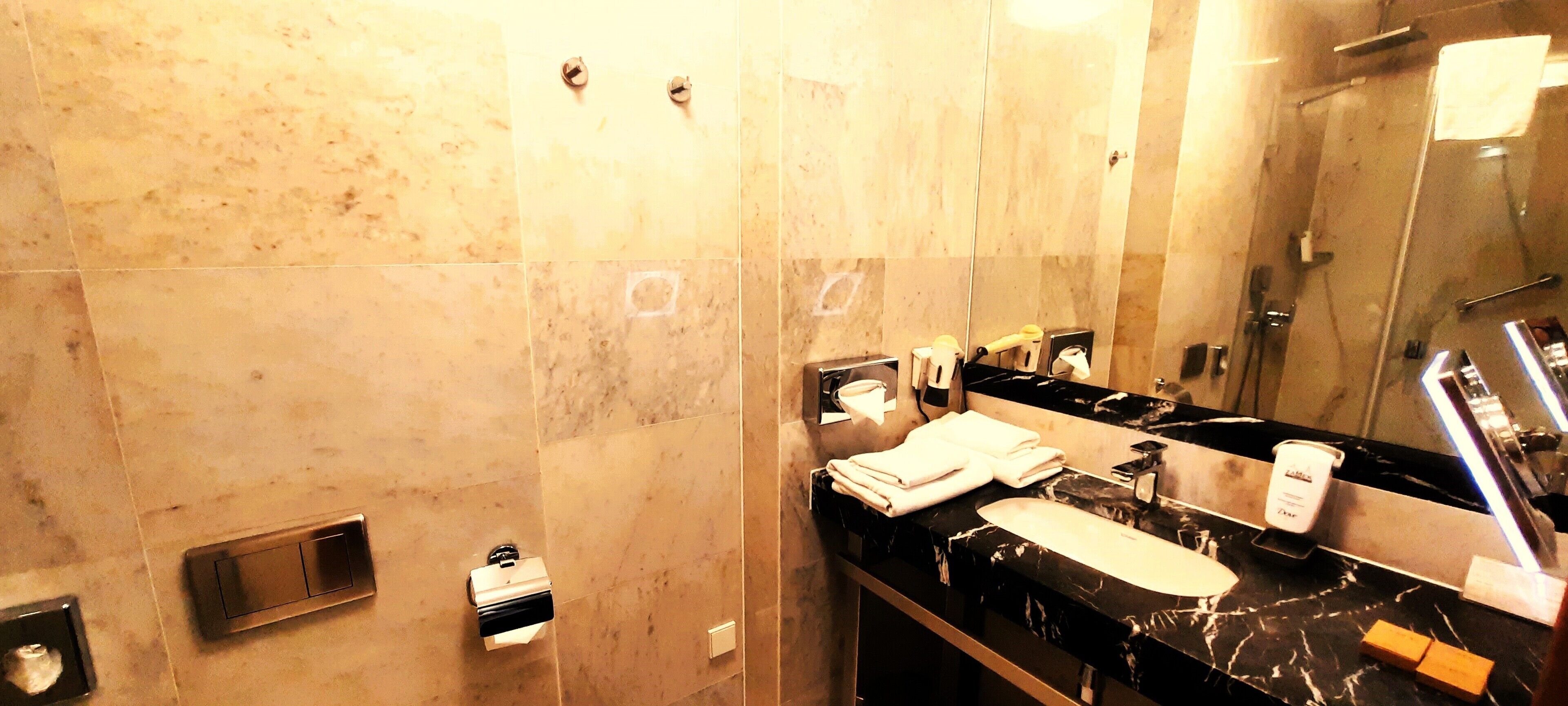 A bathroom with a marble wall, a sink, a mirror, and a shower.