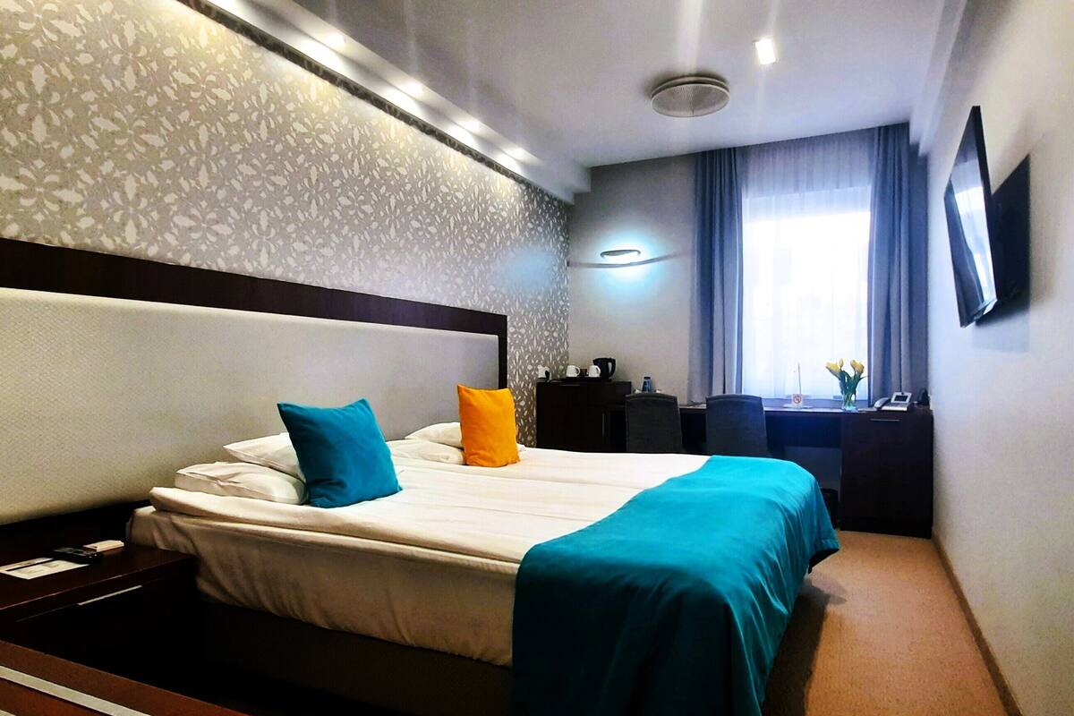 A hotel room with a bed, a desk, a chair, a TV, and a window with curtains.