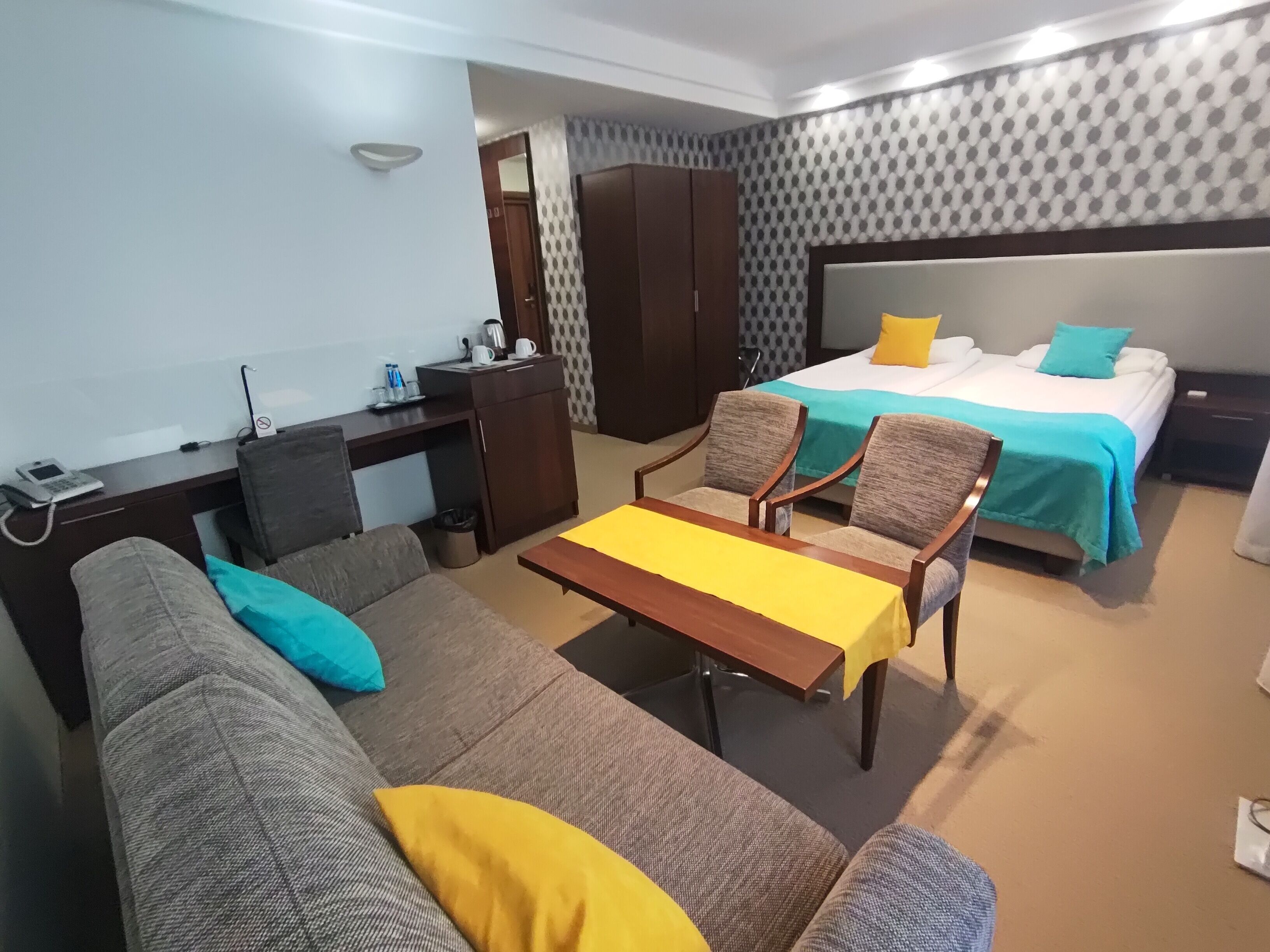 A hotel room with a bed, two armchairs, a sofa, a desk, and a small table.