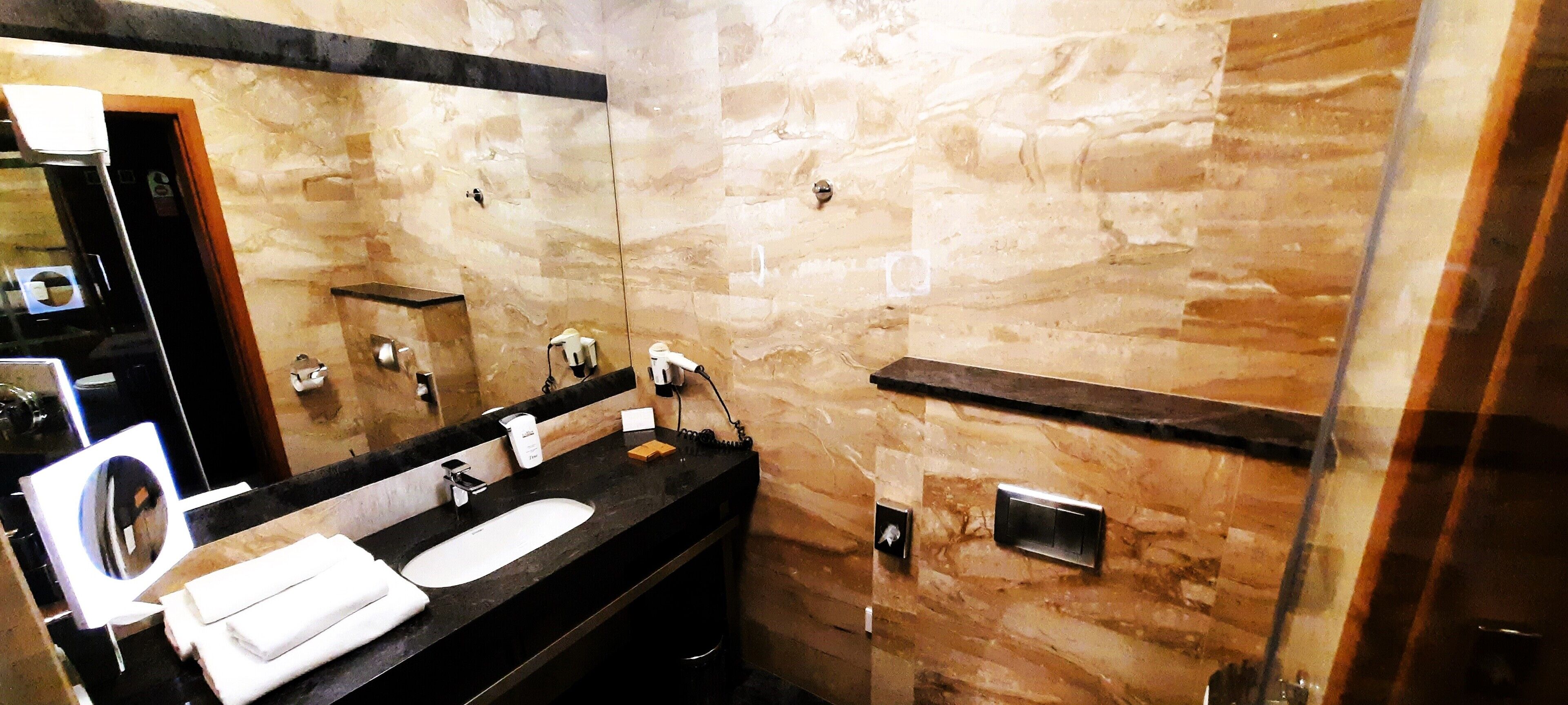 Une salle de bain avec un mur en marbre, un lavabo noir et un miroir.