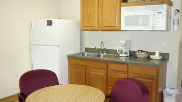 A compact kitchen with a refrigerator, microwave, sink, and a small dining table with two chairs.