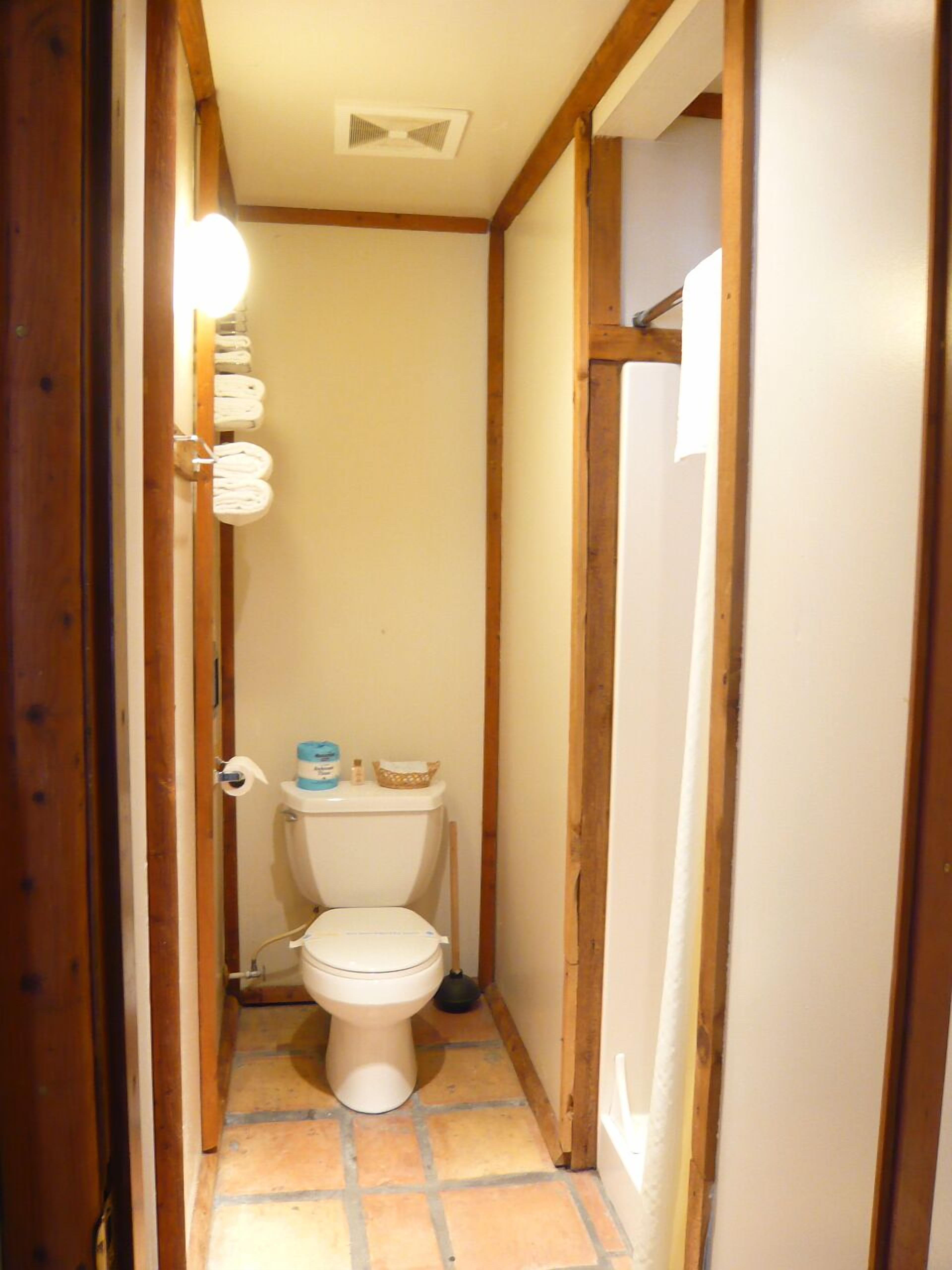 A narrow bathroom with a toilet, a roll of toilet paper, and a small shelf with toiletries.