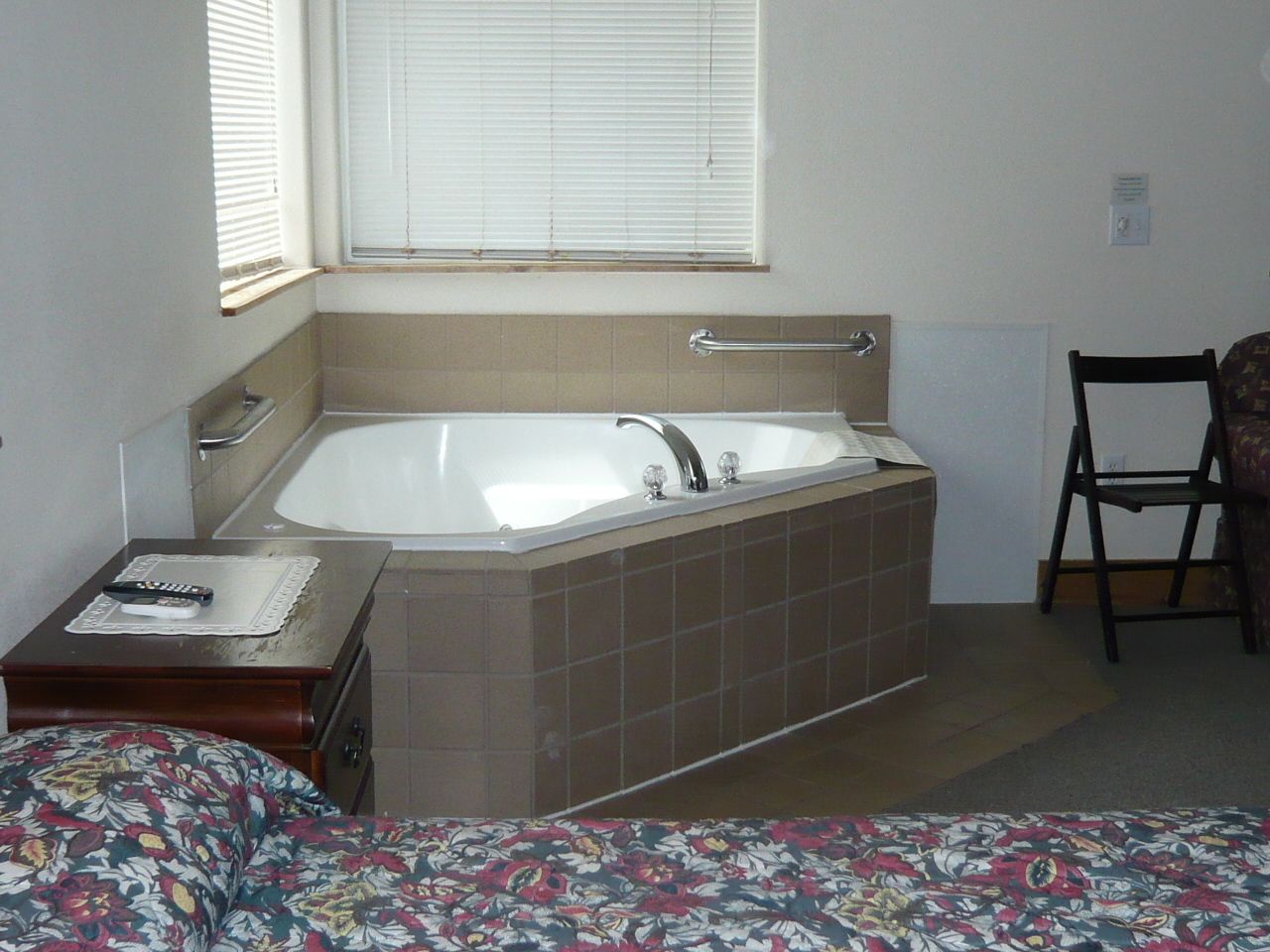 A bathroom with a bathtub, a chair, and a small table with a remote control.