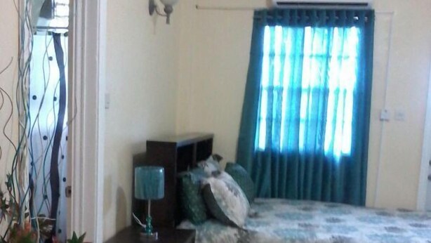 A bedroom with a bed, a nightstand, a lamp, and a window with curtains. - Summers Inn (Gros Islet)