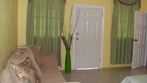 A living room with a beige sofa, a green vase, and a white door. - Summers Inn (Gros Islet)