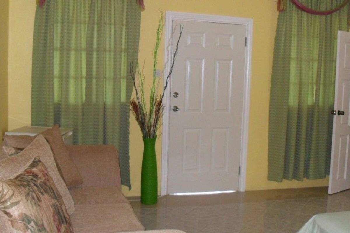 Un salon avec un canapé beige, un vase vert et une porte blanche.