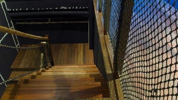 Un escalier en bois avec une rampe métallique et un mur en treillis sur un des côtés.