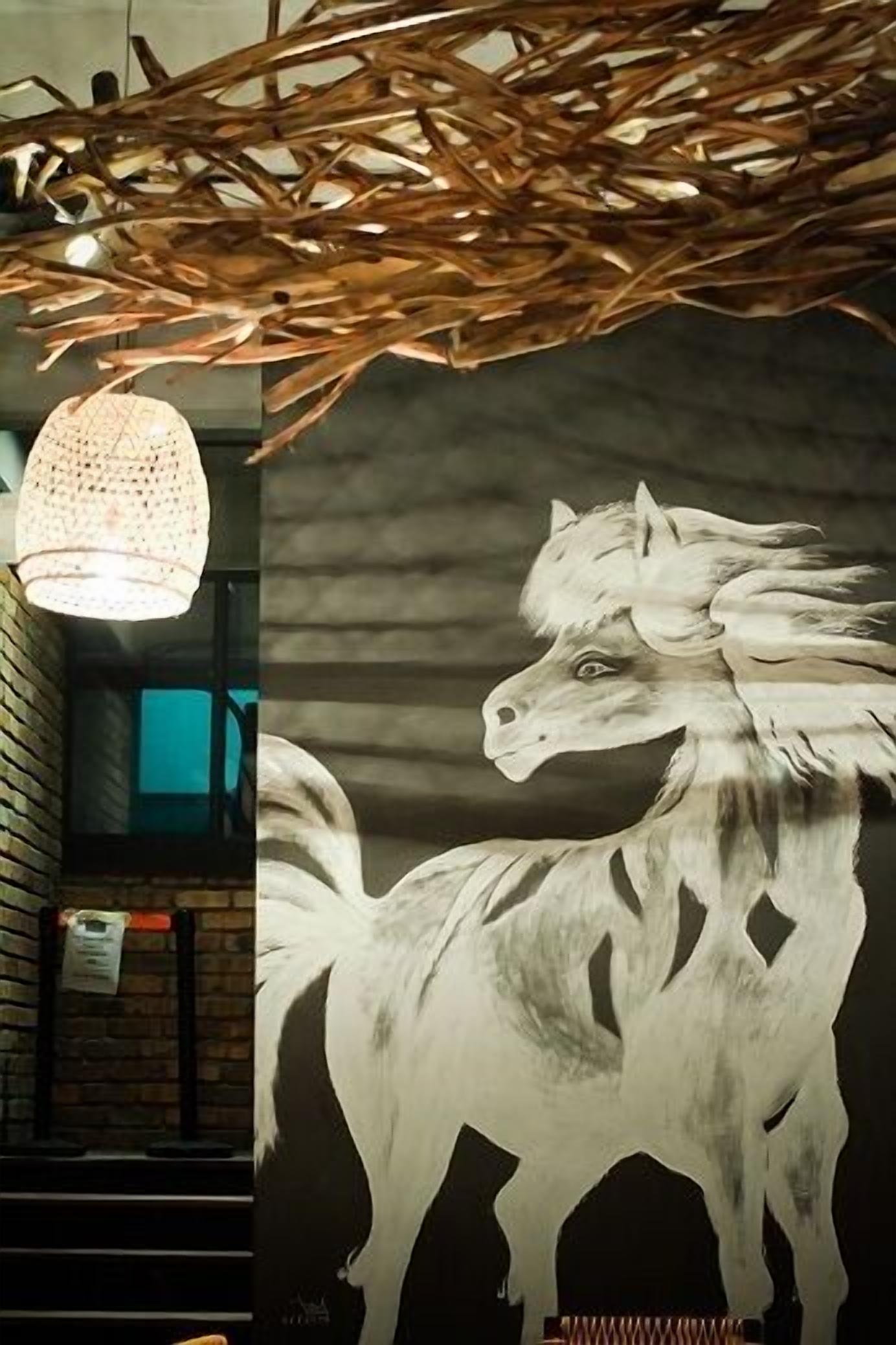 A wall mural of a white horse, a woven ceiling, and a hanging light fixture.