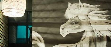 A wall mural of a white horse, a woven ceiling, and a hanging light fixture.