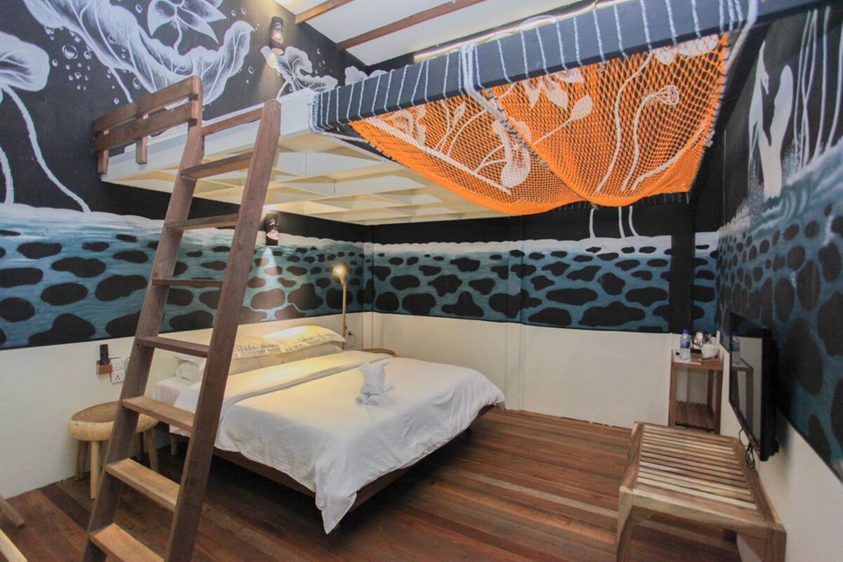 Une chambre avec un lit superposé, une échelle, une petite table et un filet orange suspendu.