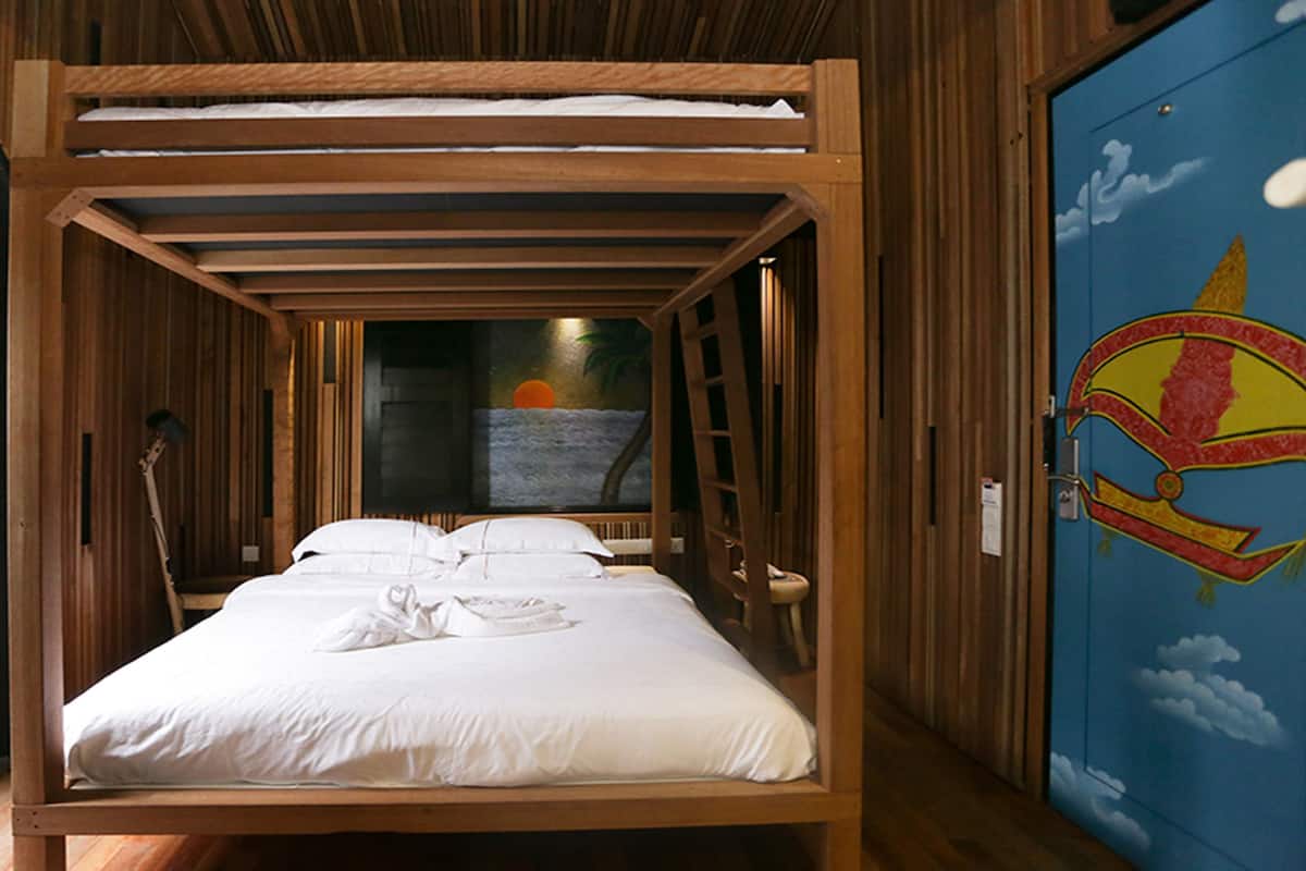 A wooden-framed bed with white linens, a ladder, and a mural of a sailboat on the wall.