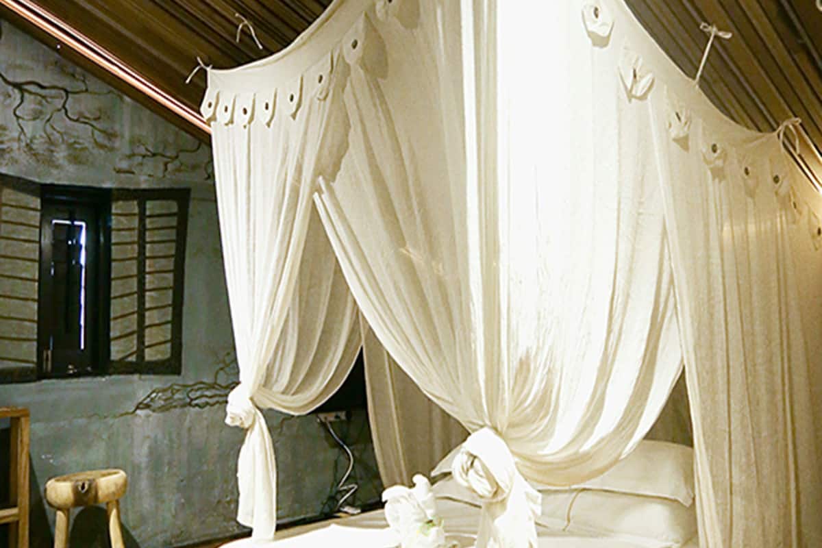 A room with a canopy bed, wooden flooring, and a stone wall with a window.