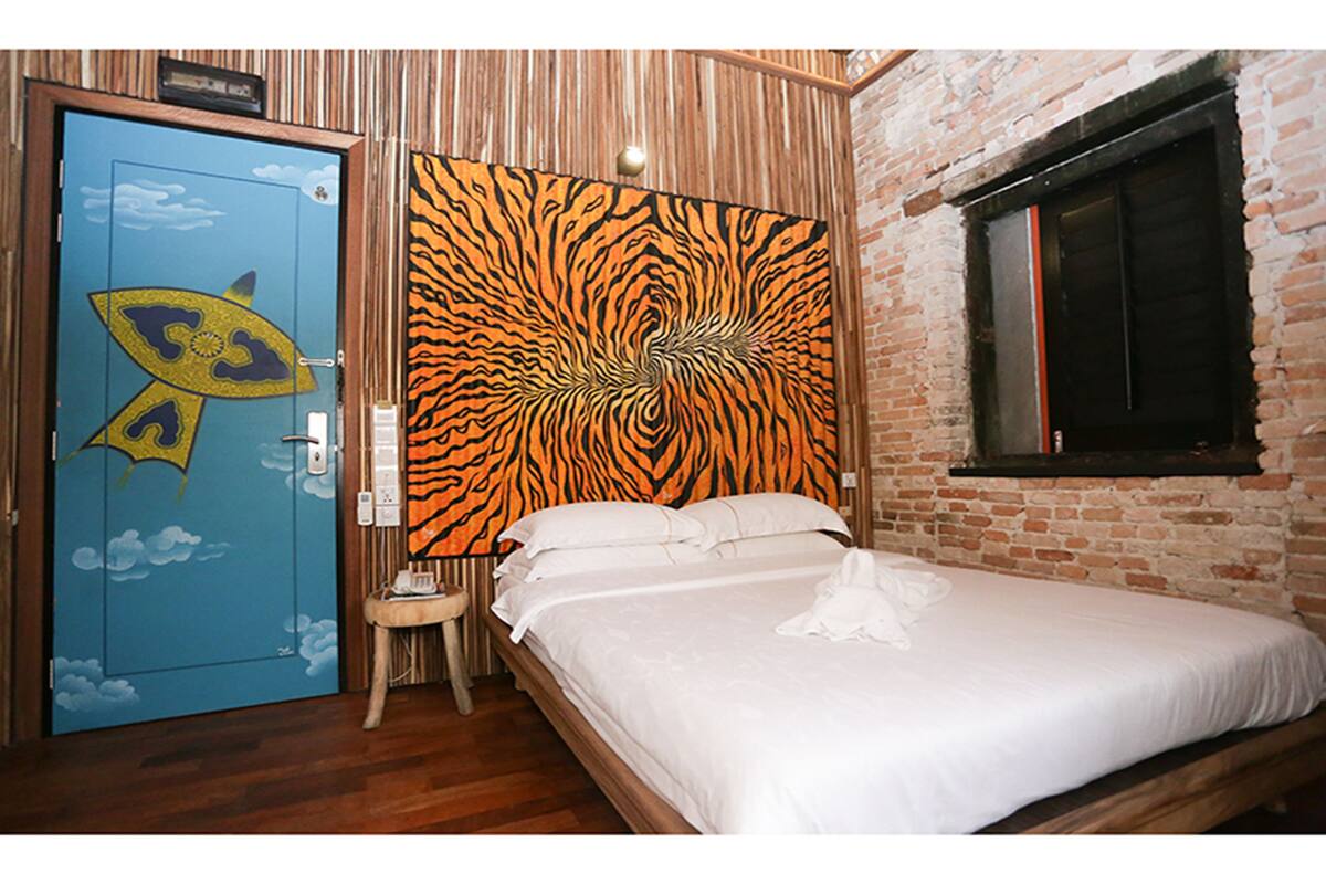 A bedroom with a bed, a blue door with a fish design, a tiger-striped headboard, and a brick wall.