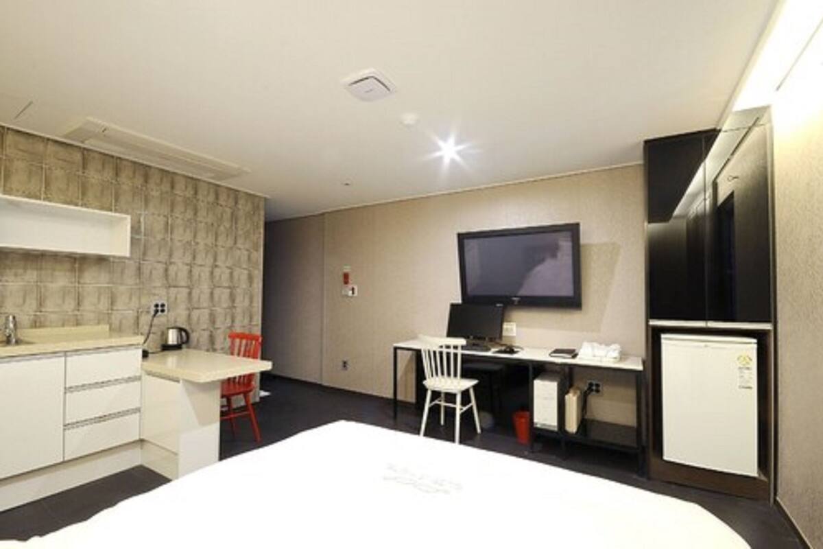 Quarto de hotel compacto com cozinha compacta, uma cama, escrivaninha com cadeira, televisão e frigorífico.