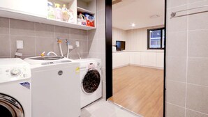 A laundry room with a washing machine, dryer, and shelves with cleaning supplies. - Queens Hotel Seomyeon Busan (Busan)