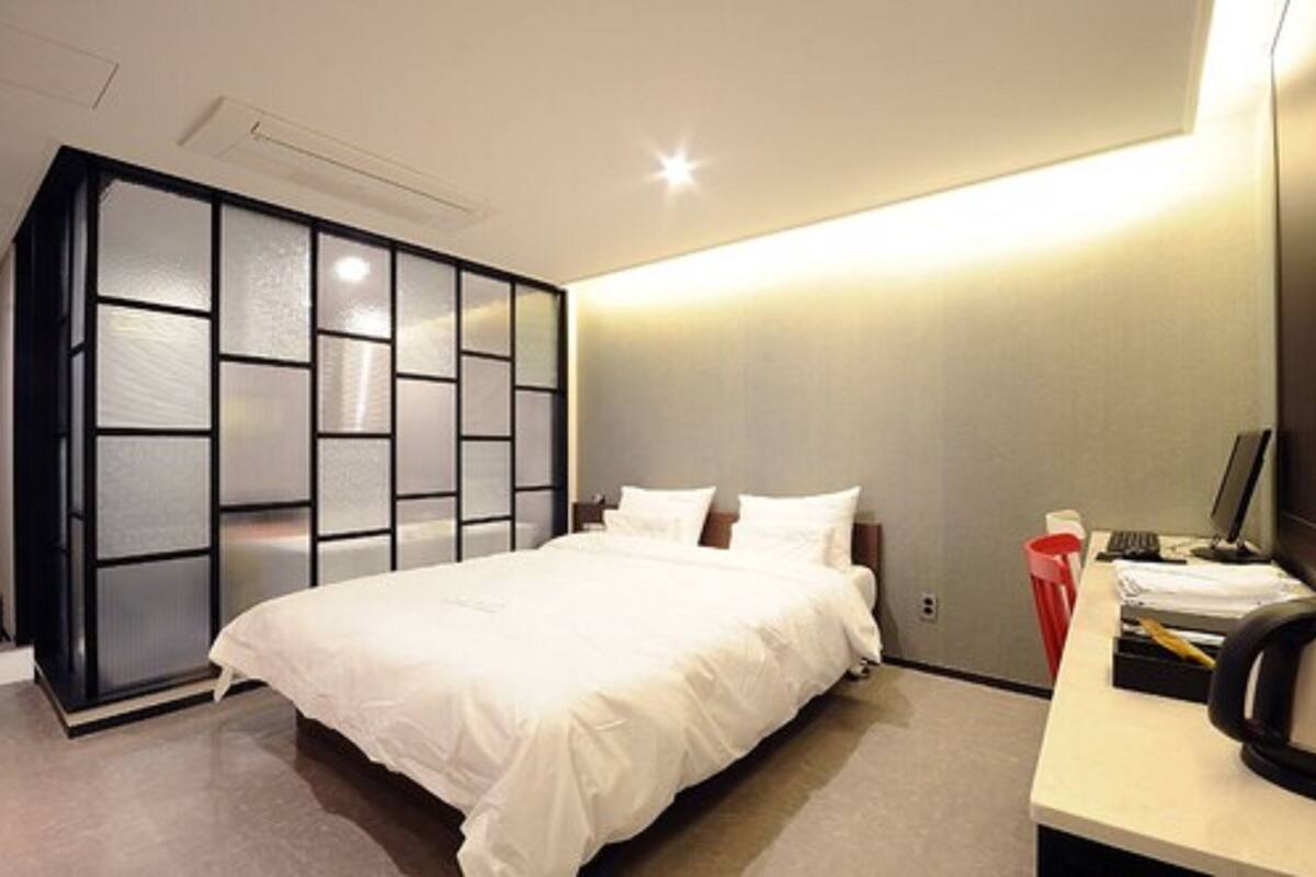 Quarto moderno com uma cama grande, uma escrivaninha com um computador e um guarda-roupa com portas deslizantes.