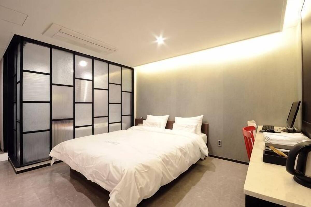 Quarto de hotel moderno com uma cama, uma escrivaninha com computador e um guarda-roupa com porta deslizante.