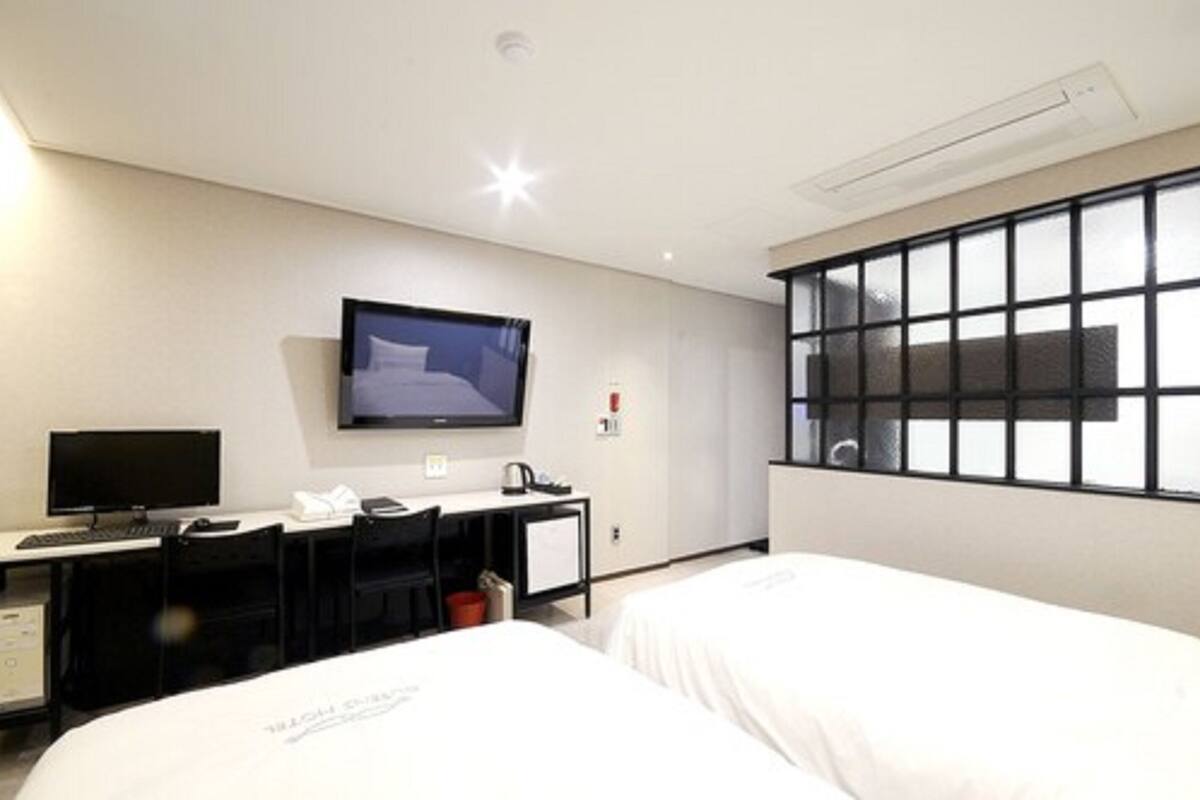 Quarto de hotel com uma cama, uma escrivaninha com computador, televisão e janela.