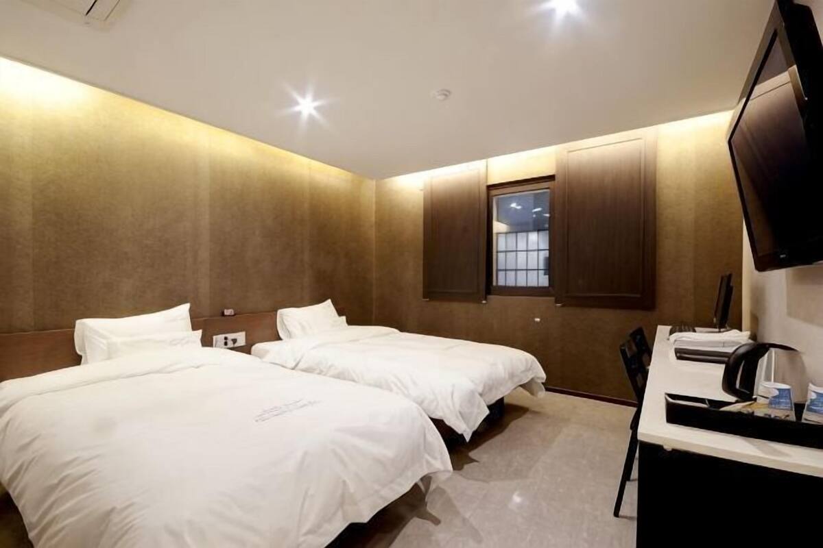 Quarto de hotel com duas camas, uma mesa de escritório e uma televisão.
