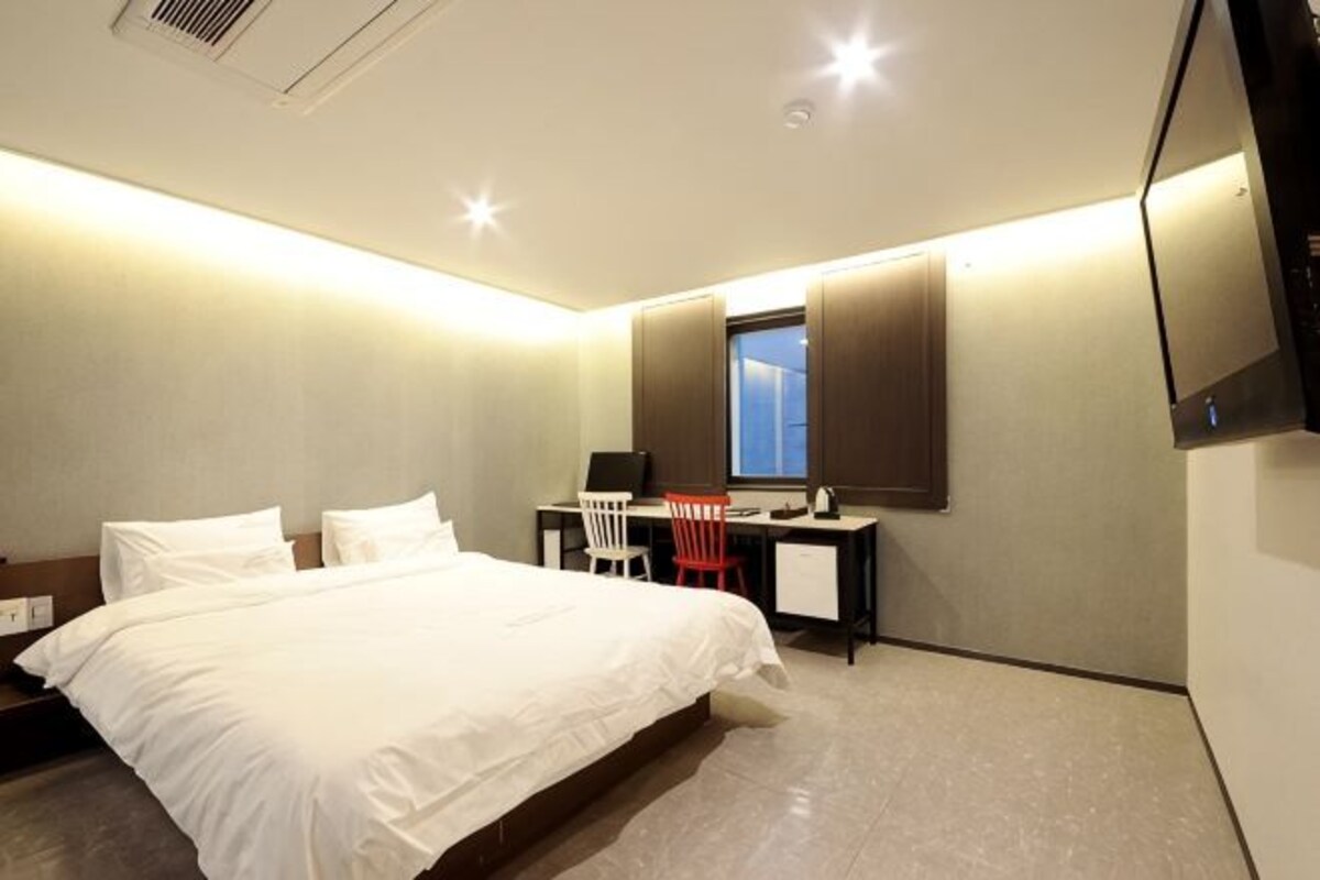 A hotel room with a bed, desk, chair, and a TV mounted on the wall.