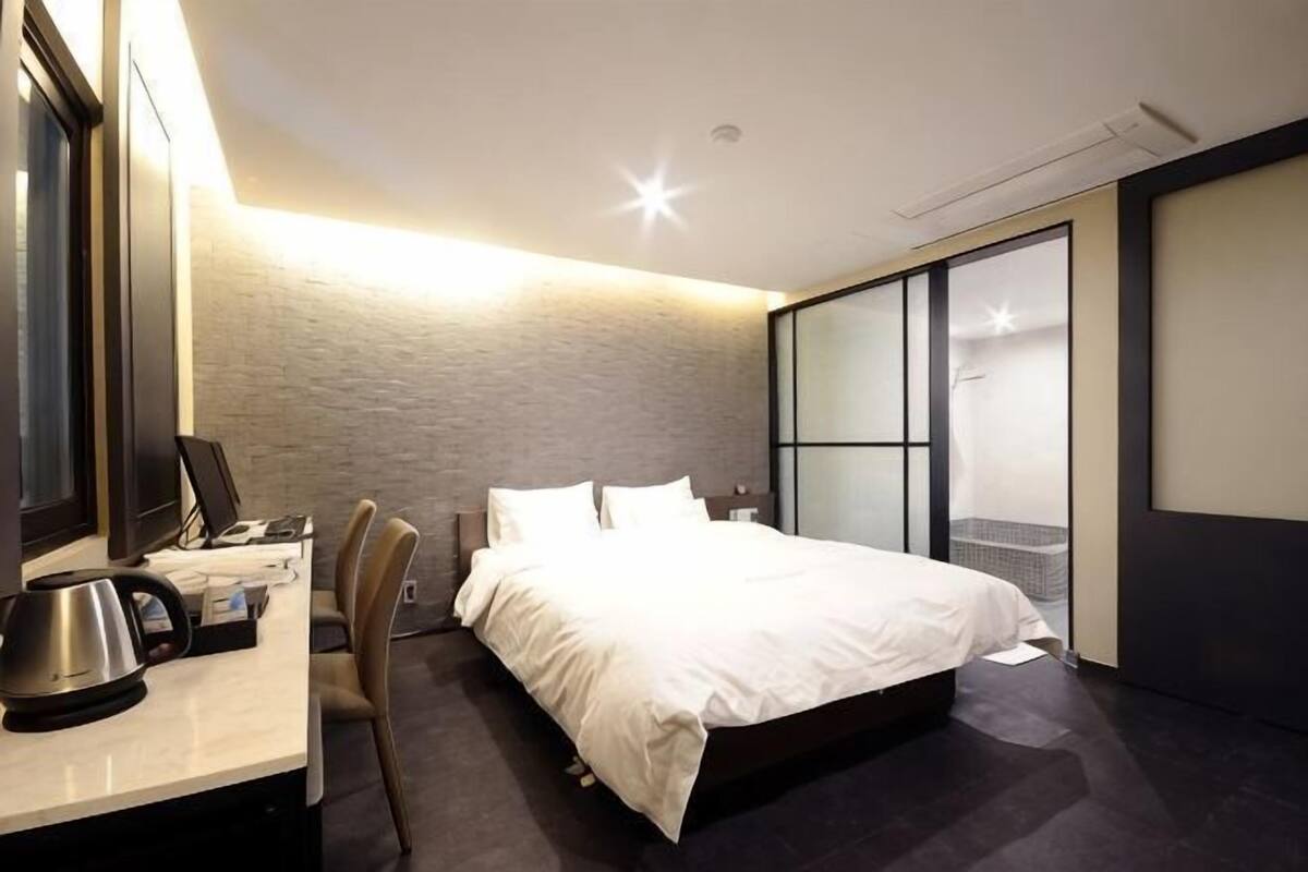 Quarto de hotel moderno com cama, escrivaninha, cadeira e uma janela grande.
