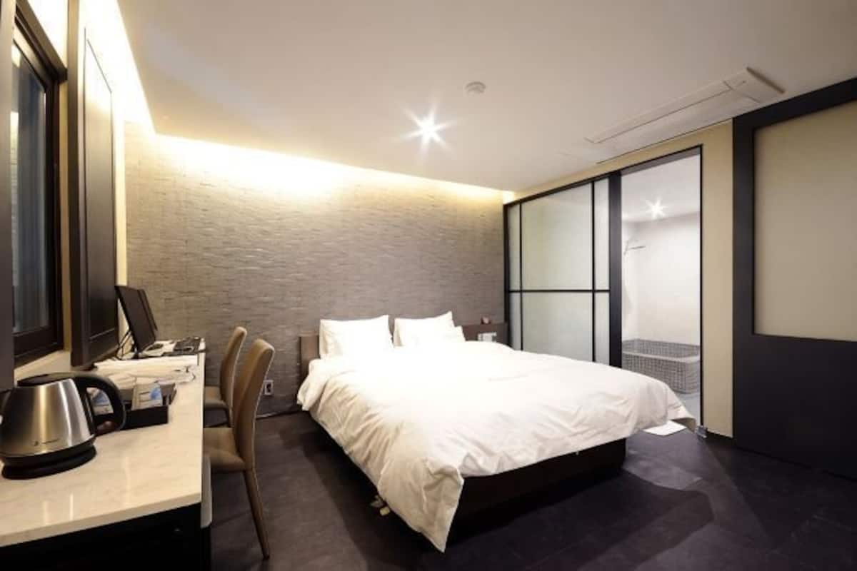 A modern hotel room with a bed, desk, chair, and a large window.