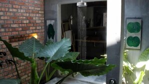 Een moderne badkamer met een bakstenen muur, een douche en grote groene planten.