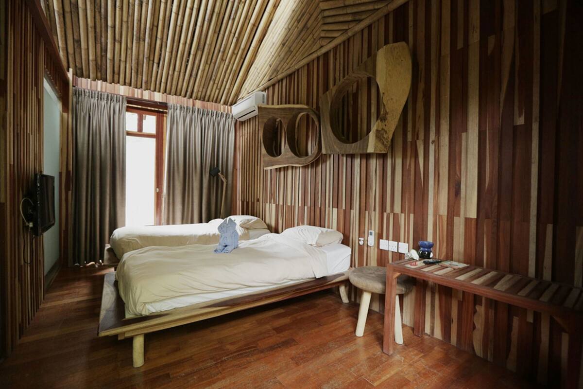 A room with a bed, a bench, a wall-mounted TV, and a window with curtains.
