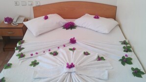 Una cama bien hecha con una decoración de toallas y flores moradas, un teléfono en la mesita de noche y una lámpara fijada a la pared.