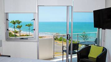 A hotel room with a large window offering a view of the beach and ocean.
