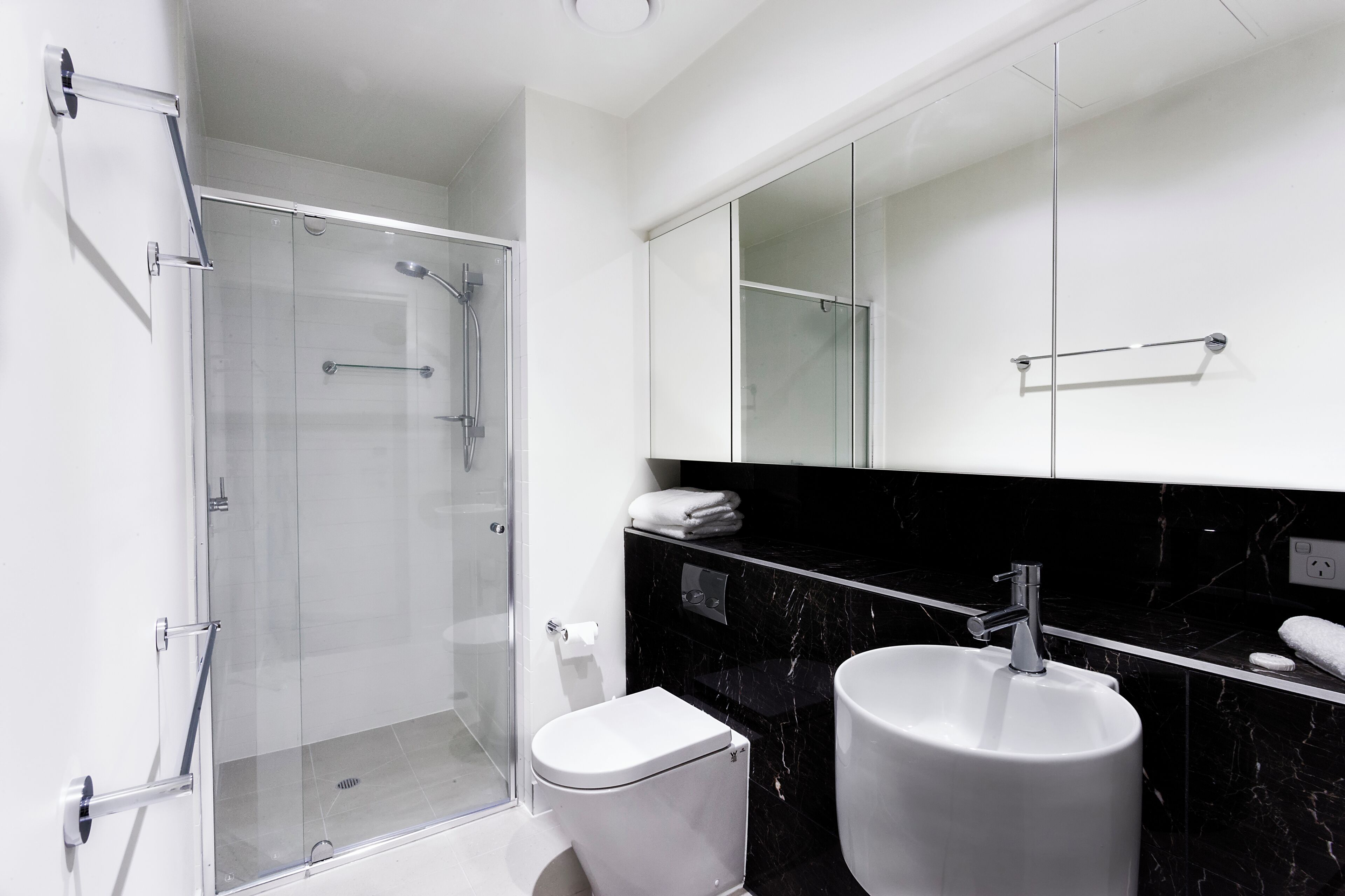 A modern bathroom with a glass-enclosed shower, a white toilet, and a black marble sink.